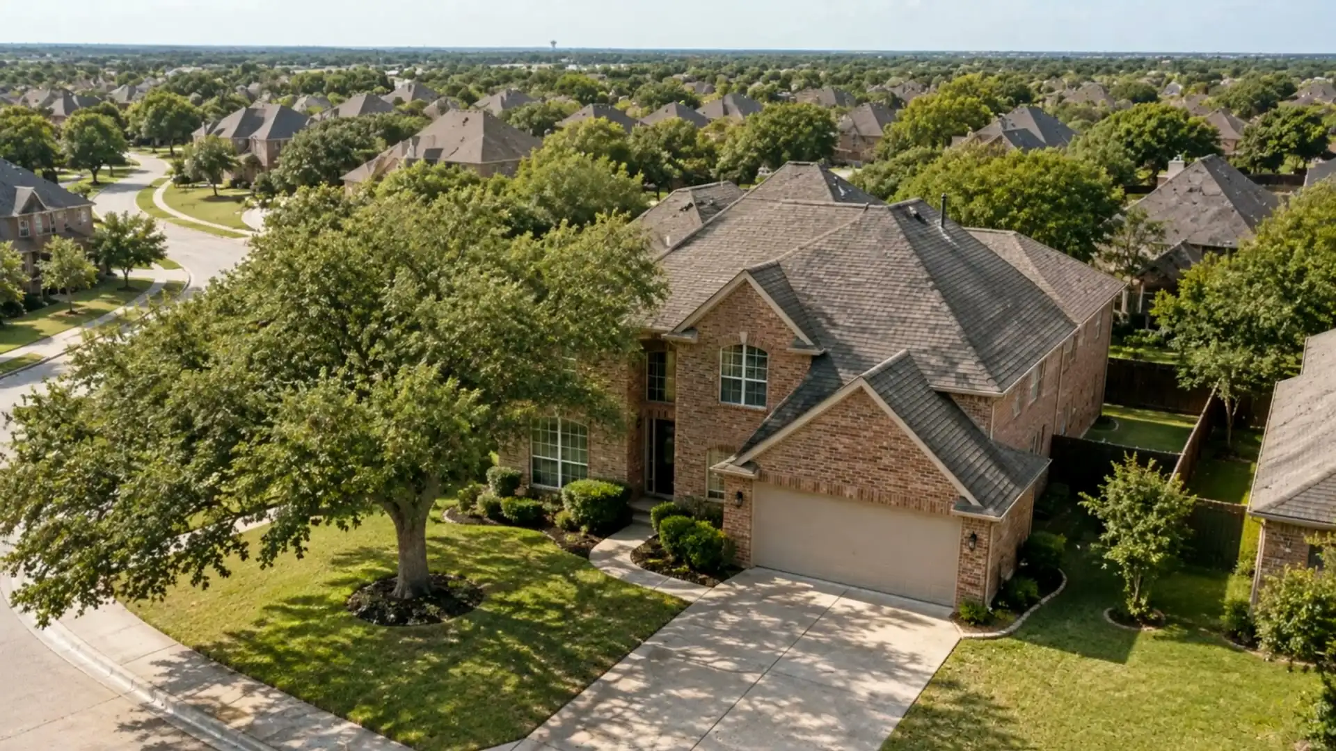 Aerial view of a brick home with a shingle roof on a tree-lined North Dallas street.