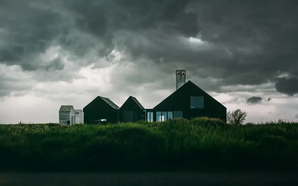 Dark storm clouds gathering over a farmhouse and a field.